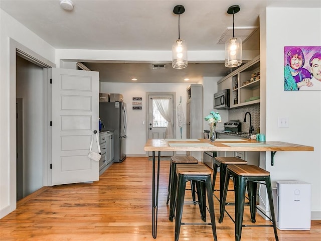 kitchen featuring a kitchen bar, stainless steel appliances, kitchen peninsula, and light hardwood / wood-style floors