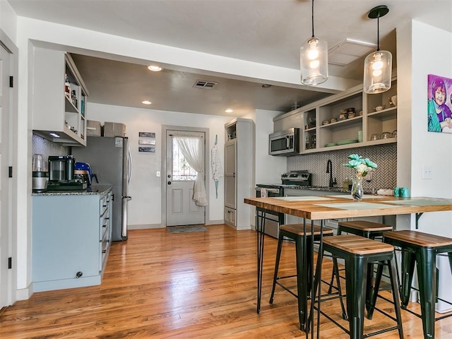 kitchen featuring appliances with stainless steel finishes, tasteful backsplash, sink, decorative light fixtures, and light hardwood / wood-style flooring