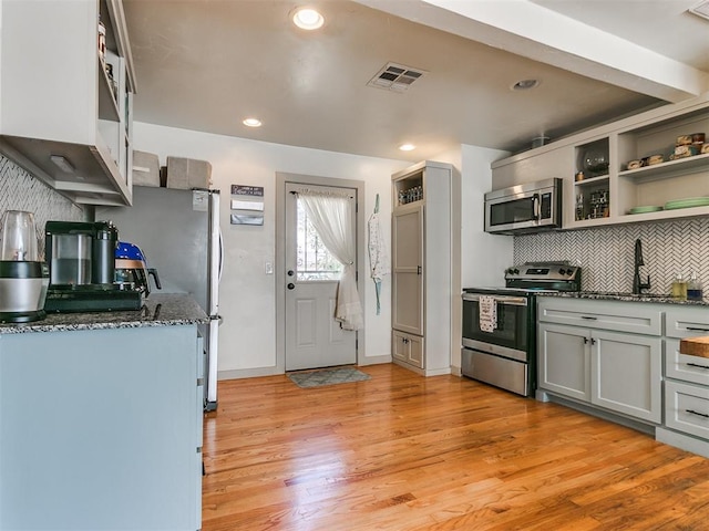 kitchen with stainless steel appliances, tasteful backsplash, light hardwood / wood-style flooring, dark stone counters, and gray cabinets