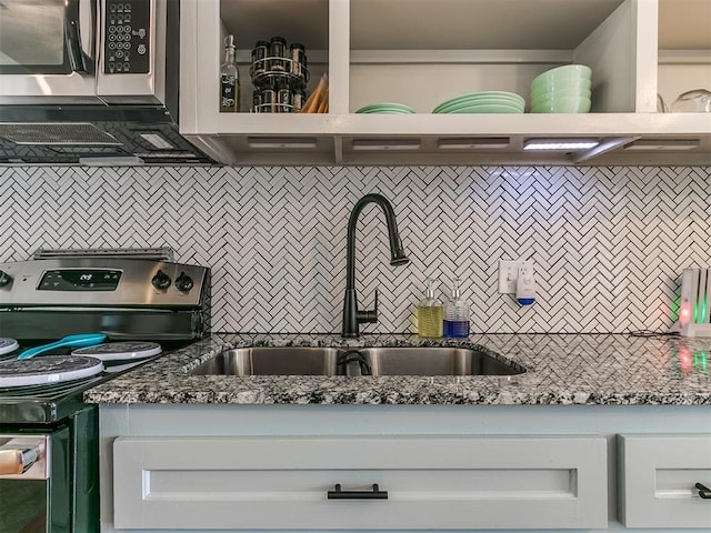 kitchen featuring stainless steel range with electric cooktop, dark stone counters, white cabinets, sink, and tasteful backsplash