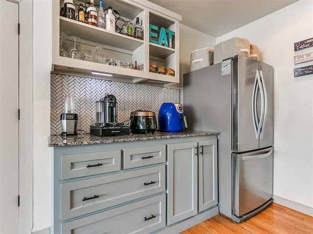 kitchen with tasteful backsplash, stainless steel fridge, dark stone counters, light hardwood / wood-style floors, and gray cabinets