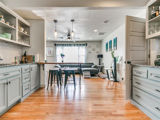 kitchen featuring light stone counters, light wood-type flooring, hanging light fixtures, and tasteful backsplash