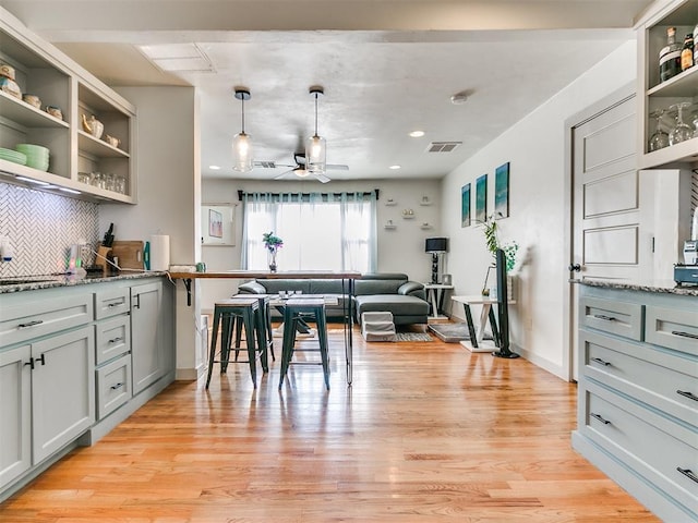 kitchen featuring backsplash, stone counters, hanging light fixtures, and light wood-type flooring