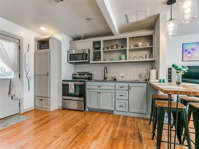 kitchen featuring gray cabinetry, hanging light fixtures, light hardwood / wood-style flooring, tasteful backsplash, and stainless steel appliances