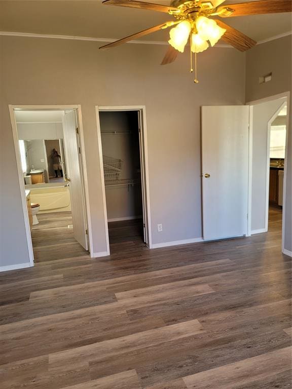 unfurnished bedroom with ceiling fan, ensuite bathroom, a walk in closet, and dark wood-type flooring