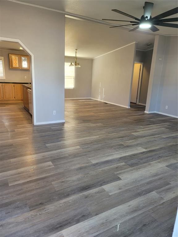 unfurnished living room with ceiling fan with notable chandelier, crown molding, and dark wood-type flooring