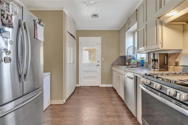 kitchen with sink, stainless steel appliances, wood-type flooring, a textured ceiling, and ornamental molding