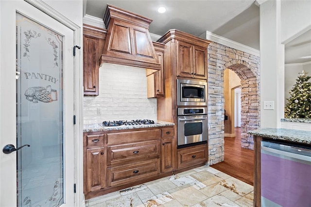 kitchen with stainless steel appliances, light stone counters, ornamental molding, and custom exhaust hood