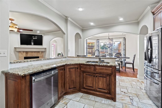 kitchen featuring sink, stainless steel appliances, light stone counters, ceiling fan with notable chandelier, and ornamental molding