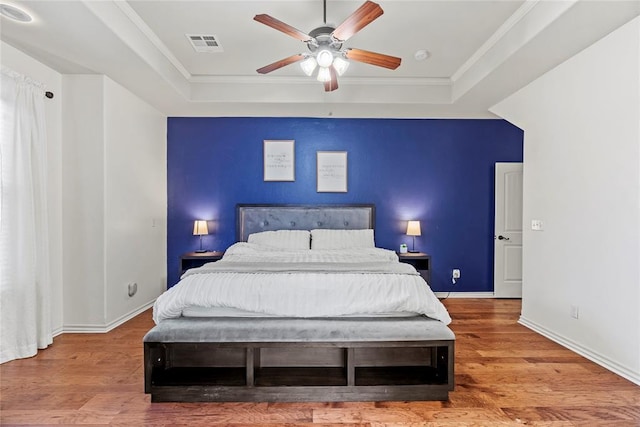 bedroom featuring hardwood / wood-style flooring, ceiling fan, a raised ceiling, and crown molding