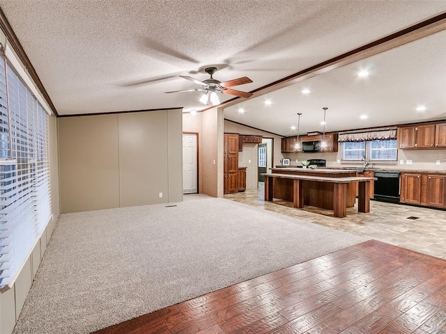 kitchen with light colored carpet, black appliances, decorative light fixtures, a kitchen island, and lofted ceiling