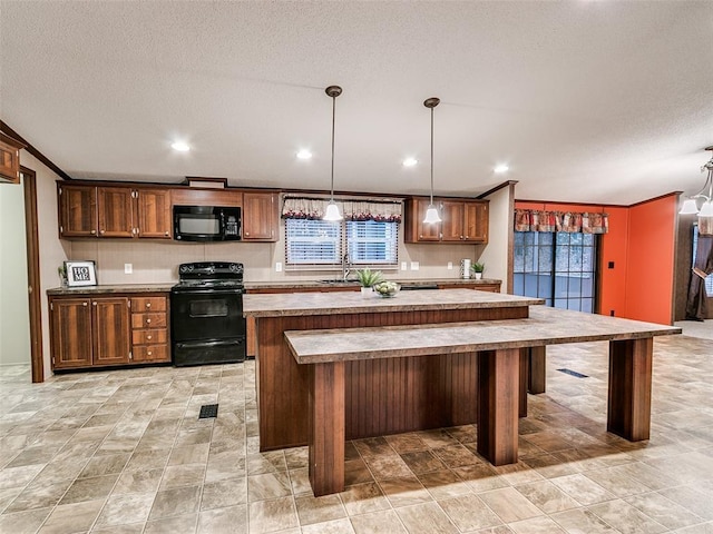 kitchen with pendant lighting, a center island, black appliances, ornamental molding, and a textured ceiling