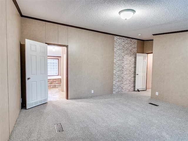 empty room with a textured ceiling, light colored carpet, and ornamental molding