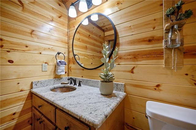 bathroom with vanity, wood walls, and toilet