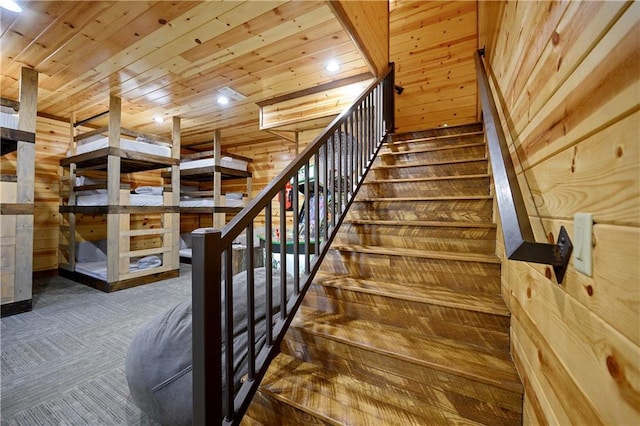 stairway with wooden walls, carpet floors, and wood ceiling