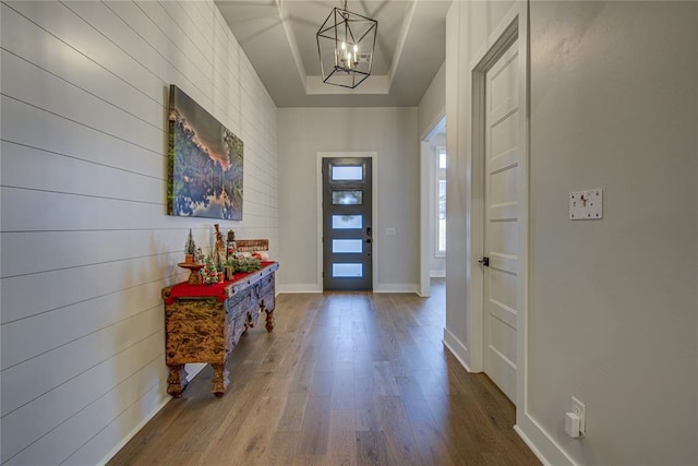 entrance foyer featuring wood-type flooring, an inviting chandelier, and a raised ceiling