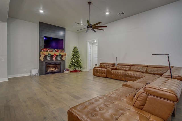 living room with hardwood / wood-style flooring, ceiling fan, and a large fireplace