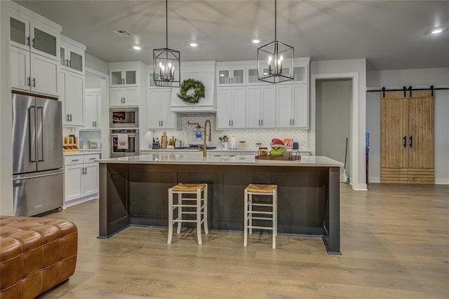 kitchen with a barn door, a center island with sink, stainless steel appliances, and light hardwood / wood-style floors