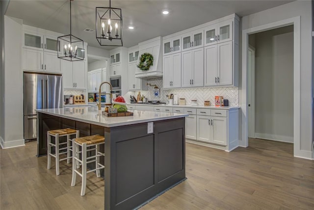 kitchen with white cabinetry, a center island with sink, stainless steel appliances, and light wood-type flooring