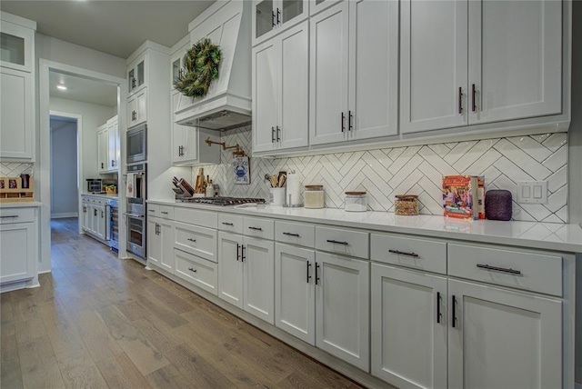 kitchen featuring appliances with stainless steel finishes, light wood-type flooring, tasteful backsplash, custom range hood, and white cabinetry