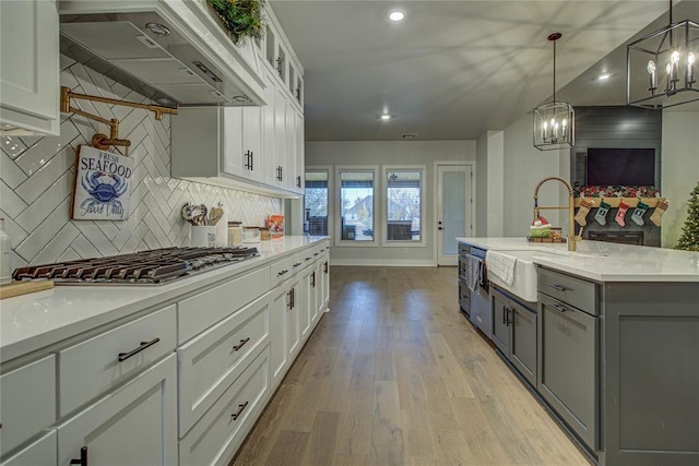 kitchen featuring white cabinetry, sink, range hood, decorative light fixtures, and a center island with sink