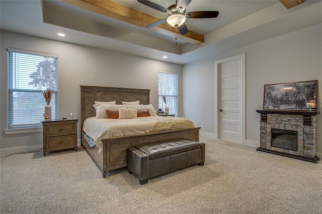 bedroom featuring a tray ceiling, ceiling fan, a fireplace, and light colored carpet