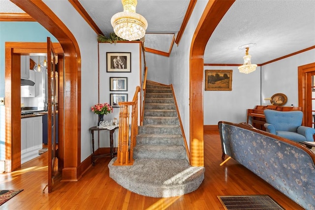 stairs with hardwood / wood-style floors, ornamental molding, a textured ceiling, and an inviting chandelier