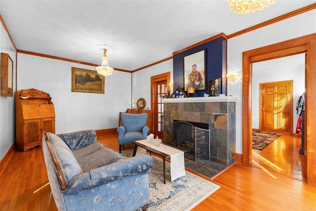 living room with wood-type flooring, a textured ceiling, a stone fireplace, and crown molding