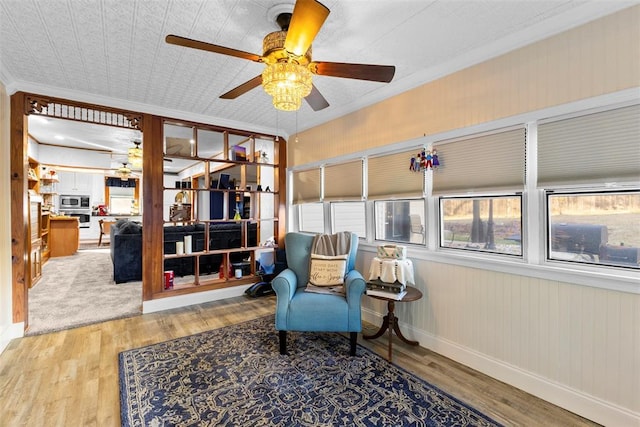 sitting room with ceiling fan, crown molding, wood-type flooring, and wood walls