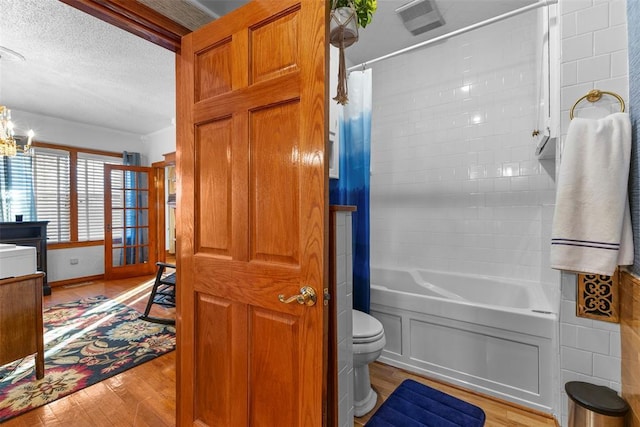 bathroom with hardwood / wood-style floors, toilet, shower / bath combo with shower curtain, a textured ceiling, and a chandelier