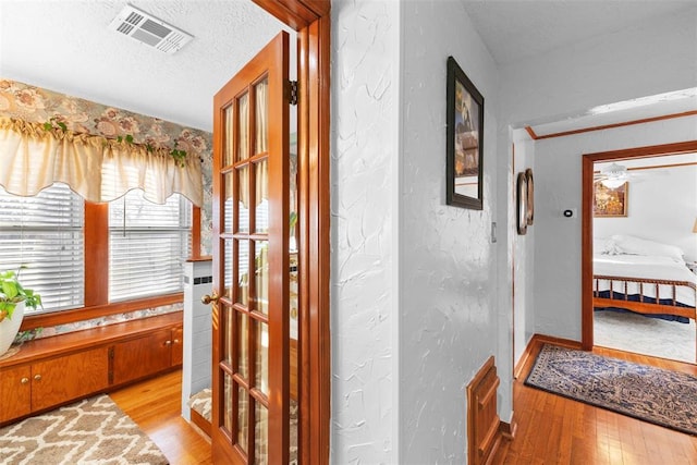 hallway with french doors, a textured ceiling, and light hardwood / wood-style floors