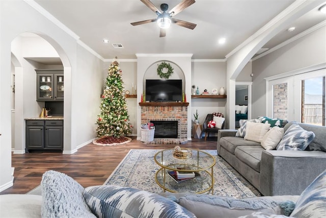 living room featuring ceiling fan, crown molding, dark wood-type flooring, and a brick fireplace