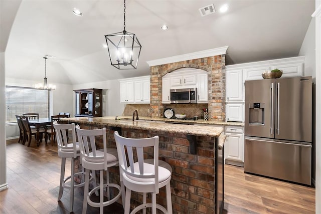 kitchen featuring lofted ceiling, white cabinetry, stainless steel appliances, and light stone counters