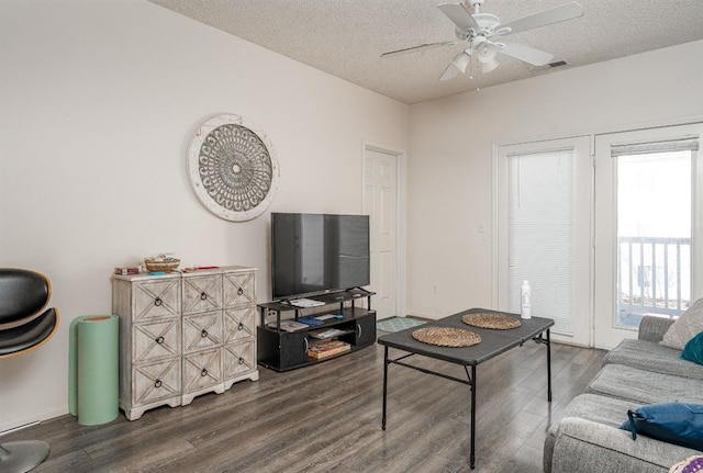 living room with a textured ceiling, ceiling fan, and dark wood-type flooring