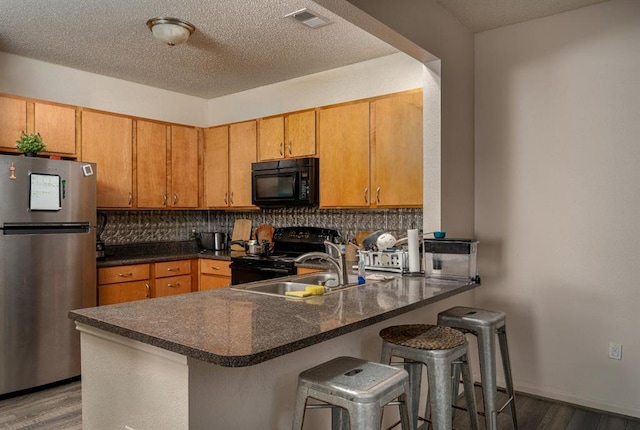 kitchen with black appliances, hardwood / wood-style flooring, decorative backsplash, kitchen peninsula, and a breakfast bar area