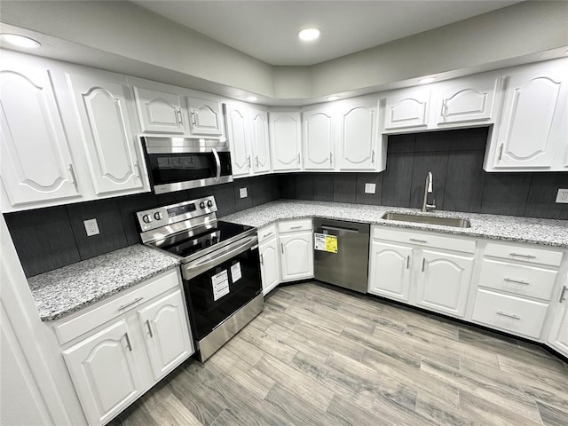 kitchen featuring white cabinets, stainless steel appliances, light stone countertops, and sink