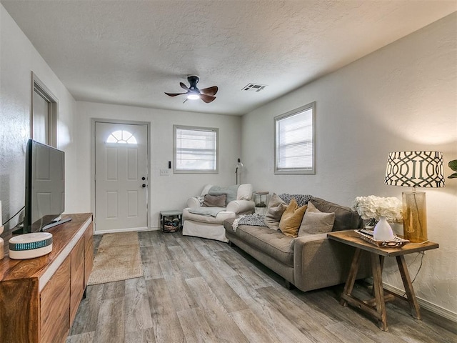 living room featuring ceiling fan, a textured ceiling, and light wood-type flooring