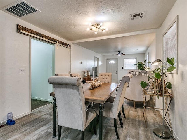 dining space featuring a barn door, ceiling fan, a textured ceiling, and hardwood / wood-style flooring