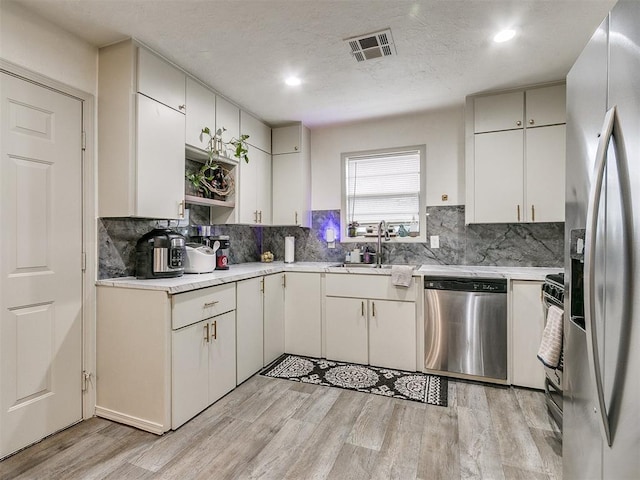 kitchen with light wood-type flooring, stainless steel appliances, white cabinetry, and sink