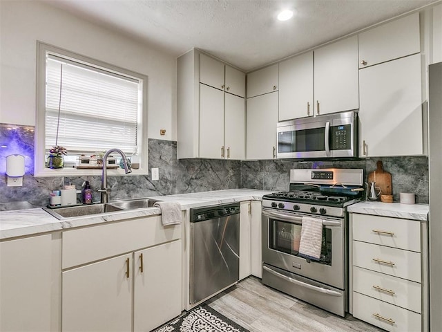 kitchen featuring appliances with stainless steel finishes, light wood-type flooring, tasteful backsplash, sink, and white cabinets