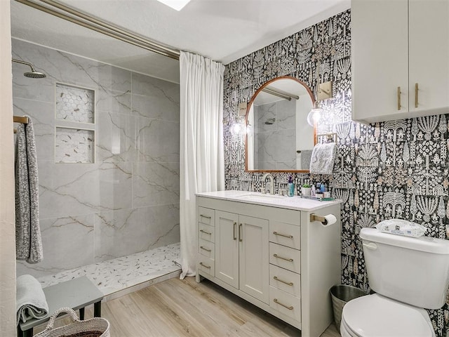 bathroom with a tile shower, hardwood / wood-style floors, toilet, vanity, and tile walls