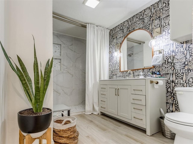 bathroom featuring toilet, wallpapered walls, a marble finish shower, and wood finished floors