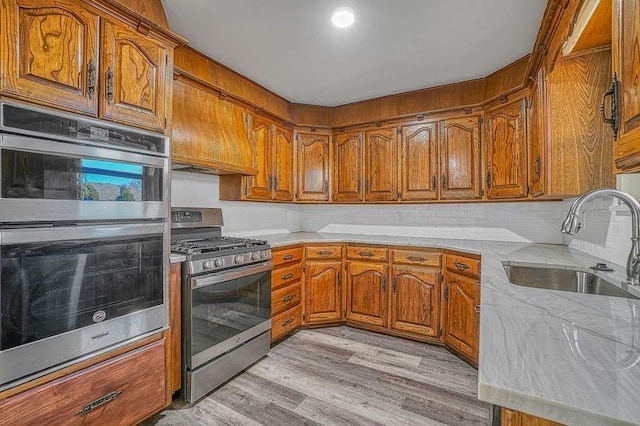 kitchen with decorative backsplash, light hardwood / wood-style floors, sink, and appliances with stainless steel finishes