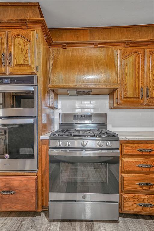 kitchen featuring tasteful backsplash, light wood-type flooring, custom range hood, and appliances with stainless steel finishes