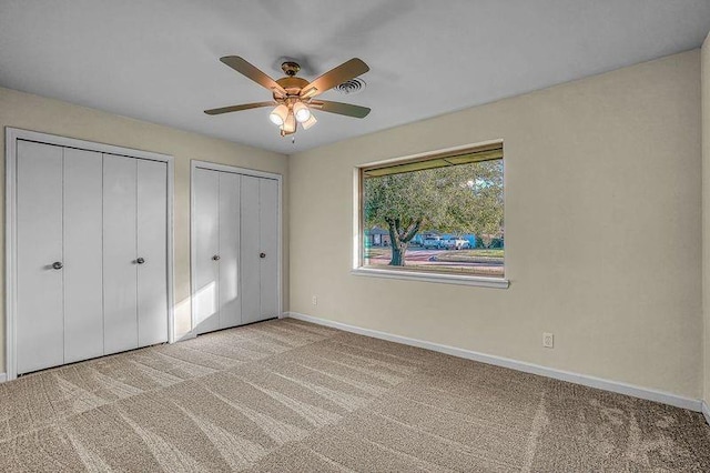 unfurnished bedroom with light colored carpet, ceiling fan, and multiple closets