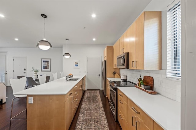 kitchen featuring a kitchen breakfast bar, stainless steel appliances, sink, dark hardwood / wood-style floors, and hanging light fixtures