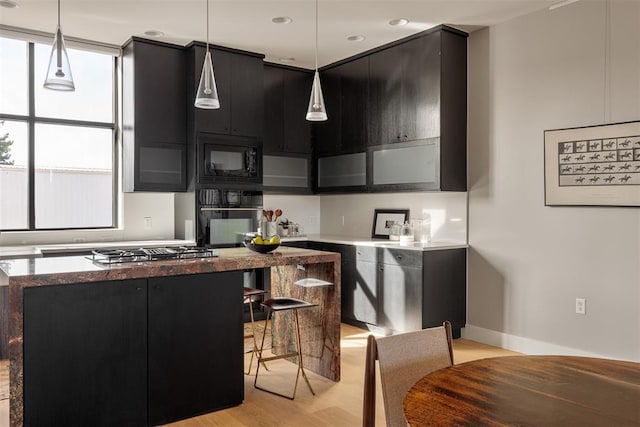 kitchen featuring a kitchen bar, decorative light fixtures, light hardwood / wood-style flooring, and black appliances