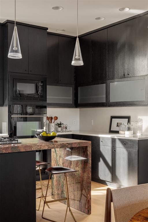 kitchen with hanging light fixtures, black appliances, and light wood-type flooring