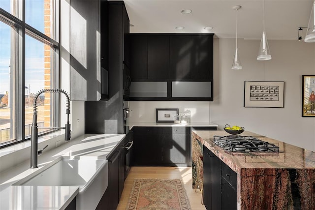 kitchen featuring stainless steel gas cooktop, sink, pendant lighting, and light hardwood / wood-style floors