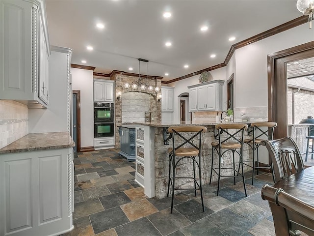 kitchen with light stone countertops, white cabinetry, kitchen peninsula, and black double oven